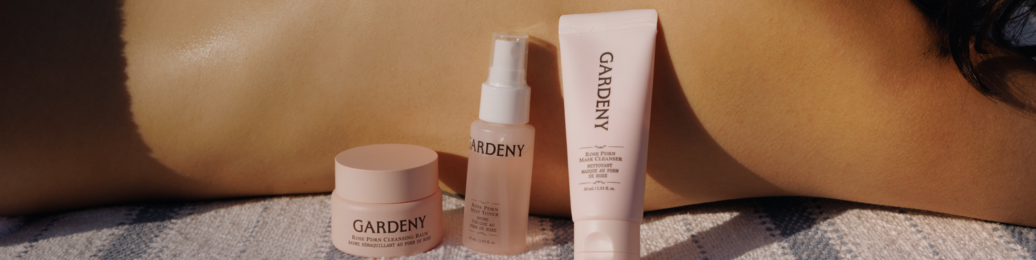 Sun-lit lifestyle banner featuring Gardény’s Rose PDRN Cleansing Balm, Mist Toner, and Mask Cleanser arranged on a textured towel beside a model’s back. Warm outdoor lighting highlights the soothing, skin-first formulas powered by plant-based Rose PDRN, positioning the trio as Gardény’s bestselling essentials for gentle cleansing, deep hydration, and naturally revived radiance.