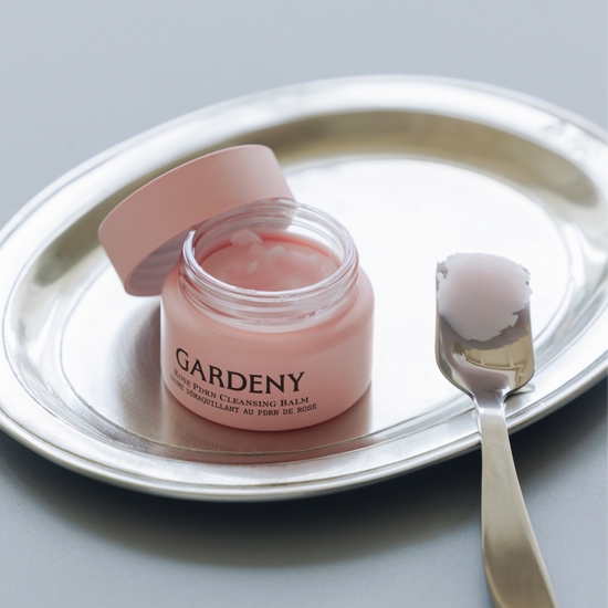 Open jar of Gardeny Rose PDRN Cleansing Balm resting on a polished silver tray with a spatula holding a scoop of its sherbet-like texture. The image highlights the balm’s melt-to-oil formula that dissolves makeup, SPF, and buildup effortlessly while infusing skin with plant-based Rose PDRN for hydration, radiance, and a refreshed, supple, comfortable finish.