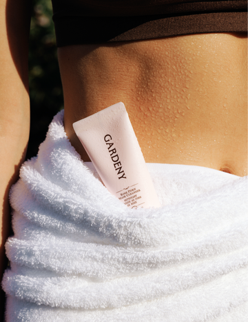 Gardeny Rose PDRN Mask Cleanser tucked into a white towel wrapped around a dewy, sunlit waist, with droplets highlighting post-shower freshness. The warm natural light reflects Gardeny’s gentle, flower-powered formulas made with plant-based PDRN for hydration and skin comfort, ideal for anyone seeking a Korean cleanser that prevents dryness while cleansing away impurities.