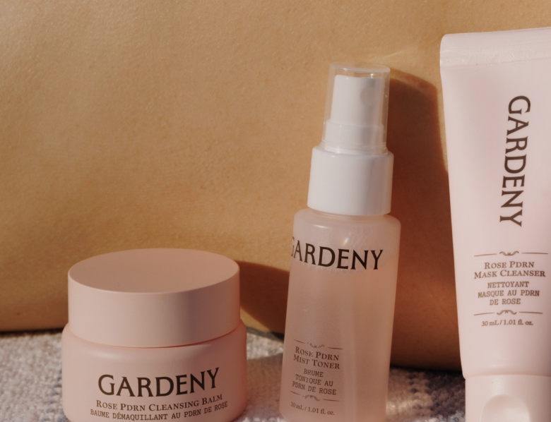 Sun-lit lifestyle banner featuring Gardény’s Rose PDRN Cleansing Balm, Mist Toner, and Mask Cleanser arranged on a textured towel beside a model’s back. Warm outdoor lighting highlights the soothing, skin-first formulas powered by plant-based Rose PDRN, positioning the trio as Gardény’s bestselling essentials for gentle cleansing, deep hydration, and naturally revived radiance.