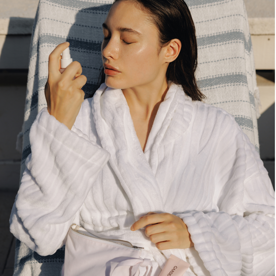 Woman in a white robe spraying the Gardeny Rose PDRN Mist Toner outdoors, showing its ultra-light, non-sticky hydration powered by plant-based Damask Rose PDRN. The scene captures a fresh, glowing finish and calming moisture ideal for on-the-go use. Designed for users wanting gentle, natural-feeling Korean hydration that refreshes dry or tight skin anytime, anywhere.