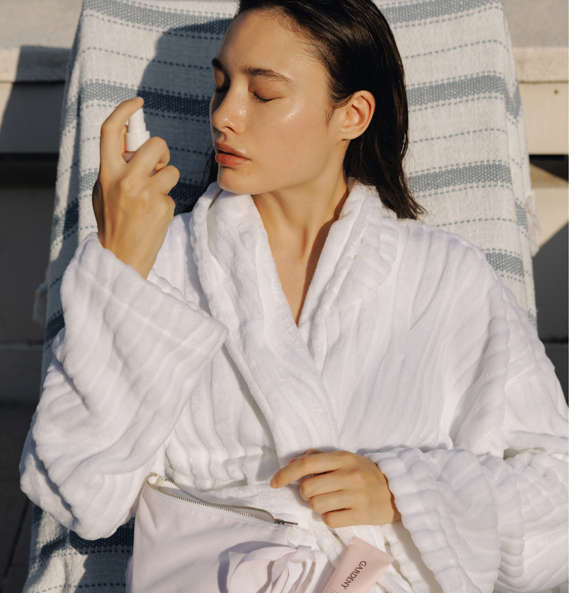 Woman in a white robe spraying the Gardeny Rose PDRN Mist Toner outdoors, showing its ultra-light, non-sticky hydration powered by plant-based Damask Rose PDRN. The scene captures a fresh, glowing finish and calming moisture ideal for on-the-go use. Designed for users wanting gentle, natural-feeling Korean hydration that refreshes dry or tight skin anytime, anywhere.