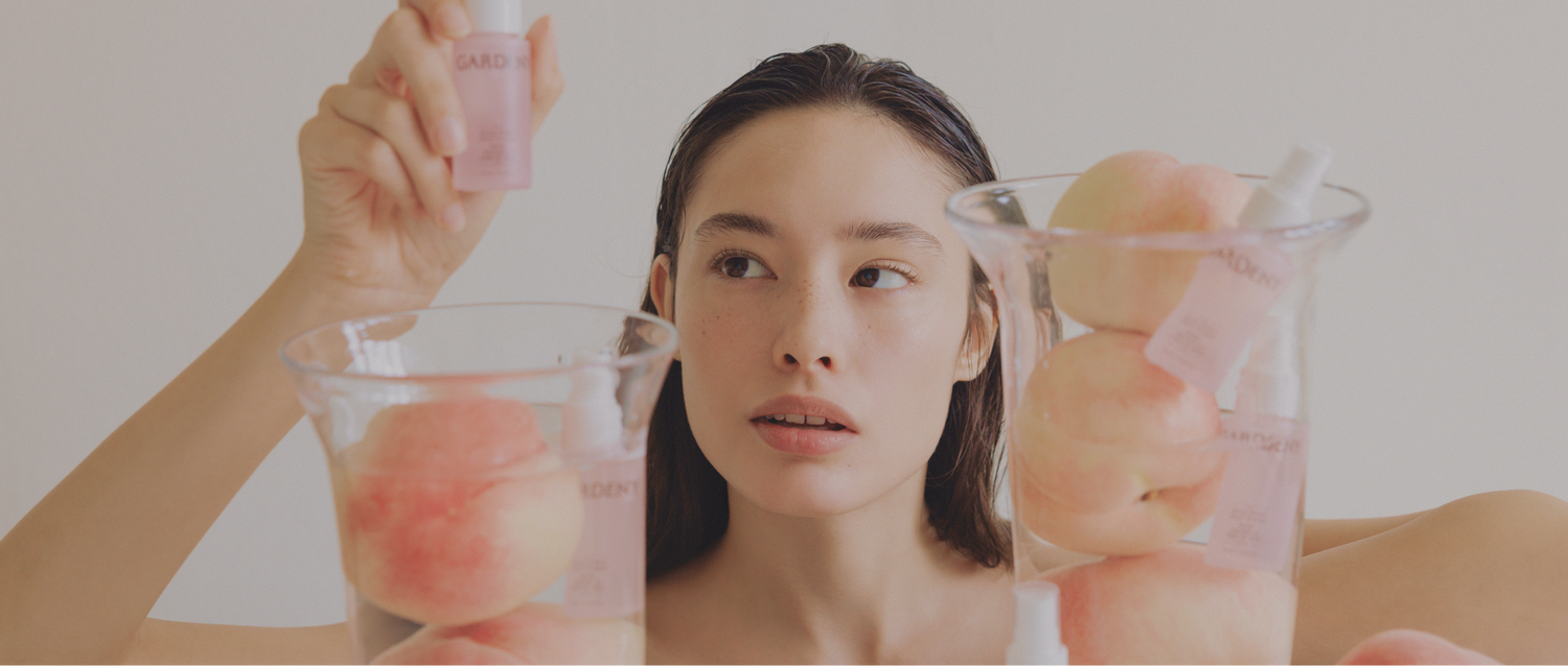 Gardeny Rose PDRN Mist Toner displayed in clear jars with fresh peaches beside a model, emphasizing its lightweight, refreshing hydration and clean Korean skincare aesthetic. The plant-based Damask Rose PDRN formula boosts moisture retention and radiance while staying non-sticky and soothing, perfect for users seeking gentle, natural-feeling PDRN toners suitable for daily or on-the-go use.