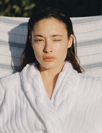Model resting outdoors in a soft robe with visibly glowing, dewy skin after applying Gardeny Rose PDRN Mist Toner. The image illustrates the lightweight yet deeply hydrating effect of plant-based Damask Rose PDRN, showing moisture-locking radiance and skin-calming benefits. Ideal for users seeking gentle Korean hydration that refreshes dry or tight skin without stickiness.