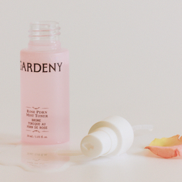 Open bottle of Gardeny Rose PDRN Mist Toner with its spray cap resting beside a soft rose petal on a gentle, fabric-like surface. Highlights Gardeny’s clean Korean plant-based PDRN formula derived from Damask rose cells, representing lightweight hydration, fast absorption, moisture retention, and a glow-enhancing, naturally floral skincare finish ideal for sensitive, dewy-skin routines.