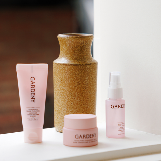 Gardeny Essential Mini Trio arranged beside a ceramic vase on a window ledge in natural light, featuring the mini mask cleanser, cleansing balm, and Rose PDRN mist toner. This setting highlights the trio’s calming, travel-ready design and its ability to restore balance, hydration, and radiance through gentle, rose-infused formulas suitable for everyday routines.