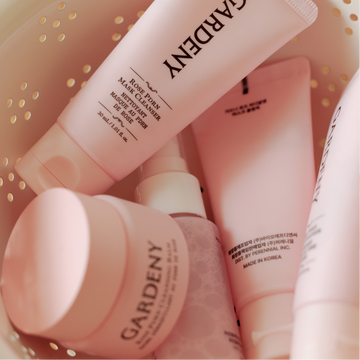 Close-up of the Gardeny Essential Mini Trio nestled inside a soft neutral basket, highlighting the compact cleansing balm, mask cleanser, and mist toner in signature pink packaging. The scene emphasizes the travel-friendly format and gentle Rose PDRN–infused formulas designed to cleanse, hydrate, and refresh the skin anytime with a soothing, rose-powered ritual.